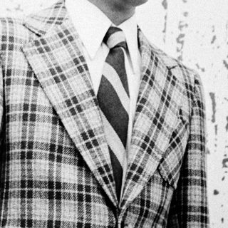 Man in plaid suit standing indoors near abstract artwork.