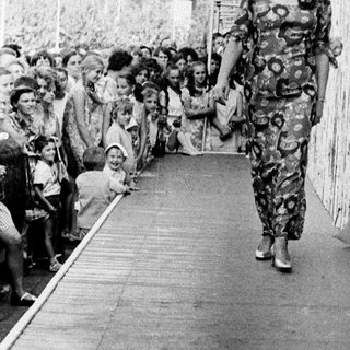 Model walks down runway in colorful patterned outfit.