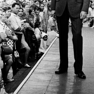 Man in suit walking past cheering crowd.
