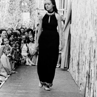 Woman walking alone in crowded outdoor corridor.