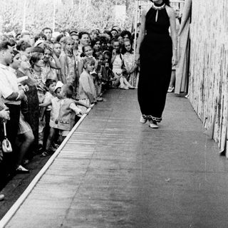 Woman walking alone in crowded outdoor corridor.