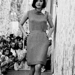 Woman walking down covered corridor amid cheering crowd.