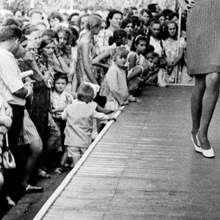 Woman walking down covered corridor amid cheering crowd.