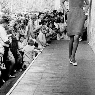 Woman walking down covered corridor amid cheering crowd.
