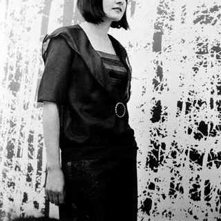 Woman in black dress posing indoors near abstract wall art.