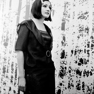 Woman in black dress posing indoors near abstract wall art.