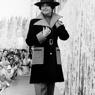 Fashionable woman walking on runway during 1960s show.