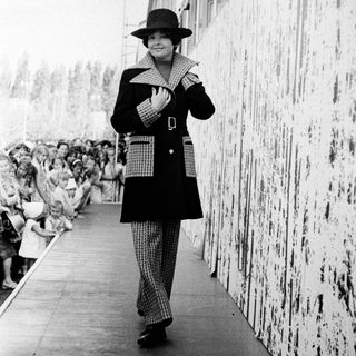Fashionable woman walking on runway during 1960s show.