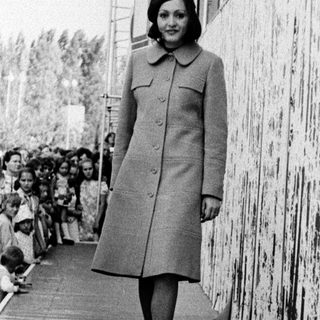 Woman in coat walking past cheering crowd.