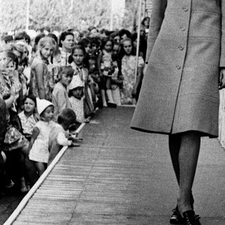 Woman in coat walking past cheering crowd.