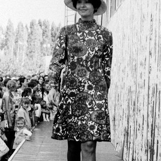 Fashion model walking on runway in floral dress.