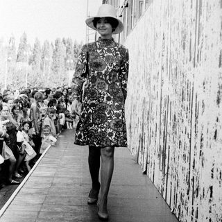 Fashion model walking on runway in floral dress.