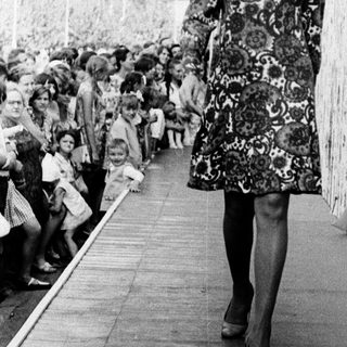 Fashion model walking on runway in floral dress.