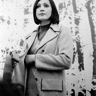 Woman in textured coat standing against abstract wall.