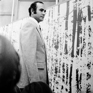 Man in suit examining abstract splatter art.