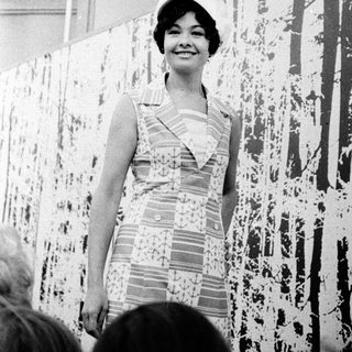Woman in 1960s dress posing at abstract art exhibition.
