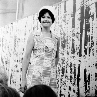 Woman in 1960s dress posing at abstract art exhibition.