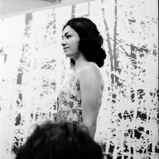 Woman speaking at an indoor event with abstract background.