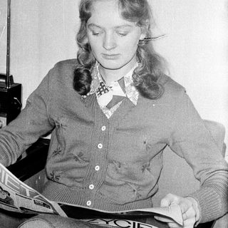 Woman reading newspaper in cozy sweater.