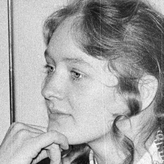 Woman in 1970s-style sweater posing thoughtfully indoors.