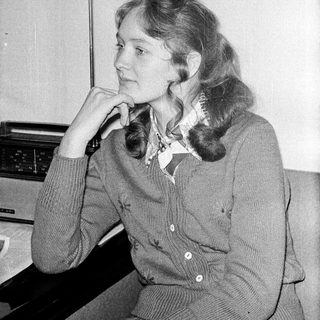 Woman in 1970s-style sweater posing thoughtfully indoors.