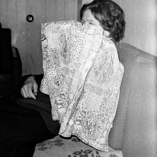 Person hiding face with patterned cloth indoors.