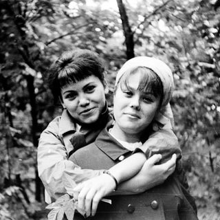 Two children hugging outdoors in a wooded area.