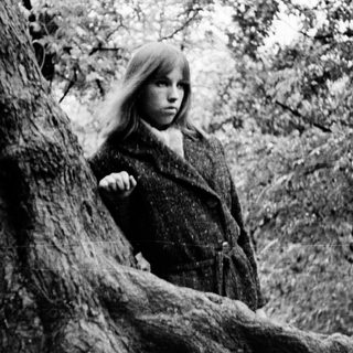 A girl standing behind a tree in a forest.
