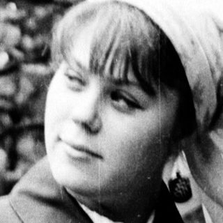 Young woman in outdoor forest setting wearing coat and headscarf.