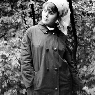 Young woman in outdoor forest setting wearing coat and headscarf.