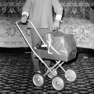 Young girl pushing toy stroller indoors.