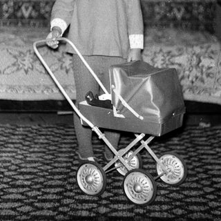 Young child pushing toy stroller indoors.