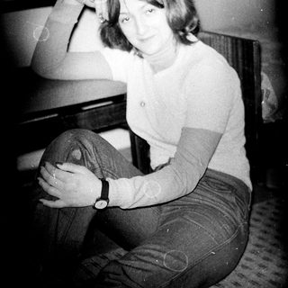 Woman sitting casually indoors, posing with arm on chair.