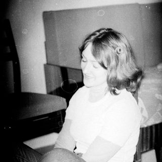 Woman sitting on bed, smiling, holding object.