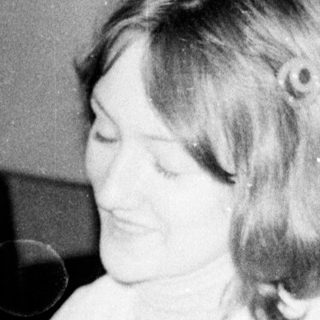 Woman sitting on bed, smiling, holding object.