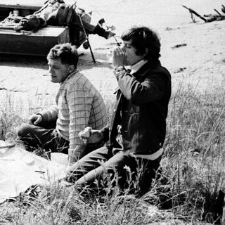 Group of people picnicking by a lake with a boat.