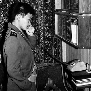 Man in uniform using vintage rotary phone.