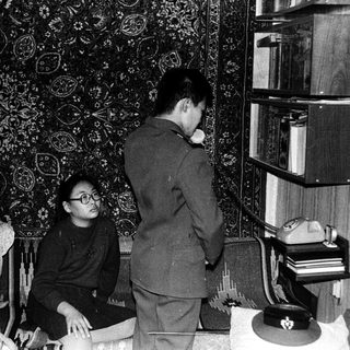 Family members in 1960s-style living room with bookshelf.