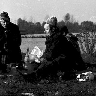 Group of people gathered outdoors by a lake, preparing food.