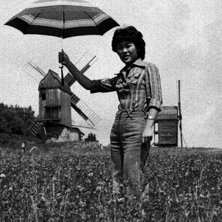 Woman holding umbrella in windy field with windmill.