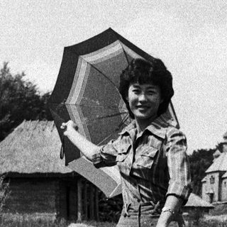 Woman holding large umbrella in rural outdoor setting.