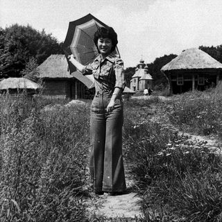 Woman holding large umbrella in rural outdoor setting.