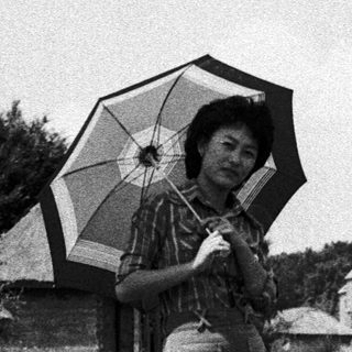 Woman holding umbrella in rural countryside setting.