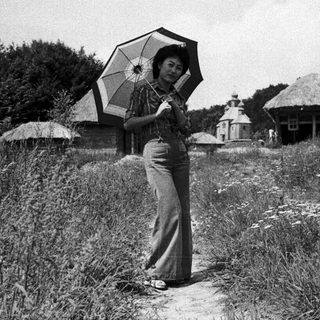 Woman holding umbrella in rural countryside setting.