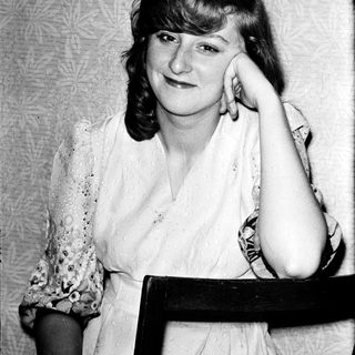 A woman posing thoughtfully indoors, resting her chin on her hand.
