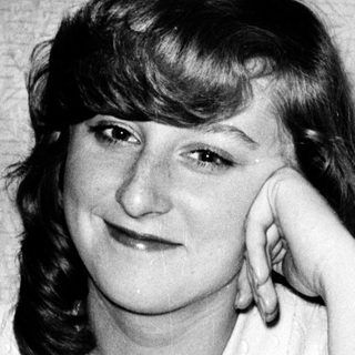 A woman posing thoughtfully indoors, resting her chin on her hand.