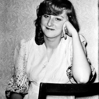 A woman posing thoughtfully indoors, resting her chin on her hand.
