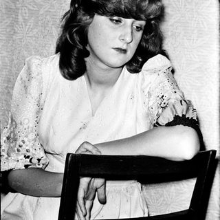 Woman sitting thoughtfully in vintage-style chair.