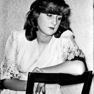 Woman sitting thoughtfully in vintage-style chair.