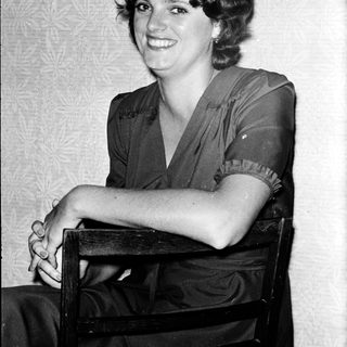 Young woman smiling in vintage-style dress, seated.